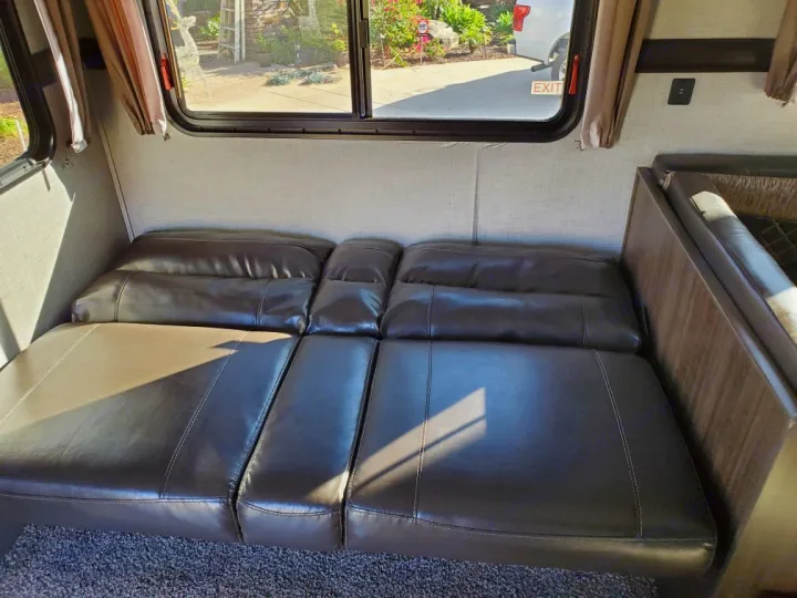RV rental interior: A dark brown convertible sofa/bed in an RV, ideal for lounge or sleeping. Windows offer outdoor views.. Crossroads Zinger 2018