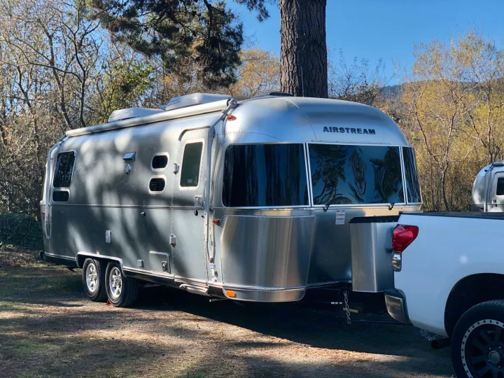 A silver Airstream RV connected to a white truck, parked outdoors among trees, ready for an RV rental getaway.. Airstream Flying Cloud 2019