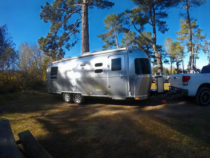 Silver Airstream travel trailer parked in a sunny campground, hitched to a truck. Explore nature with an rv rental.. Airstream Flying Cloud 2019
