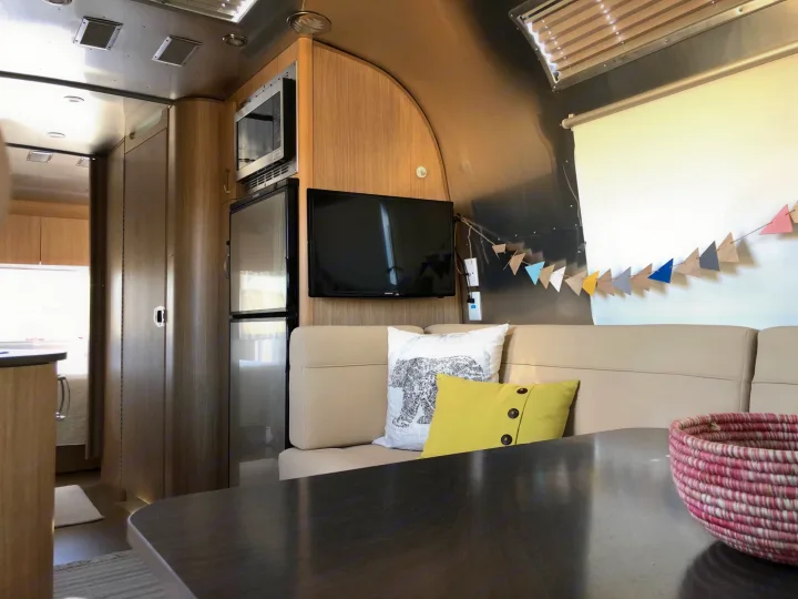 Bright RV rental interior featuring a modern kitchen, comfortable sofa with TV, and dining table with woven basket.. Airstream Flying Cloud 2019