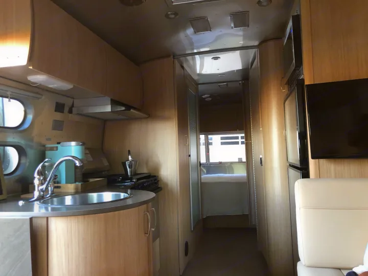 Modern RV rental interior: kitchen with sink & stove, hallway, and a comfortable bedroom. Ready for travel.. Airstream Flying Cloud 2019