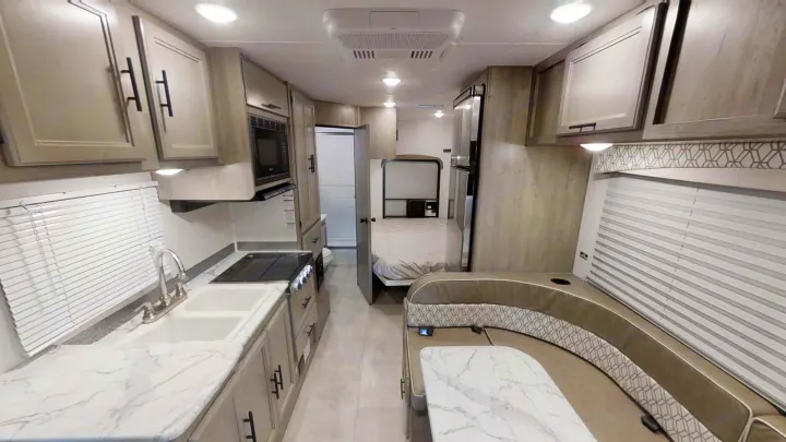Modern rv rental interior showcases a kitchen, bedroom, and dinette with light wood cabinets and marble counters.. Coachmen Freelander 2021