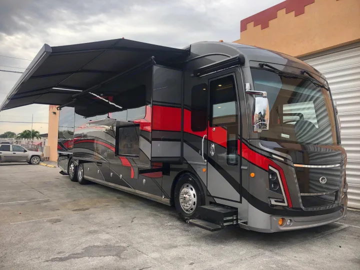 Sleek gray and red luxury motorhome for RV rental, with awning and steps deployed.. Monaco Signature 2020