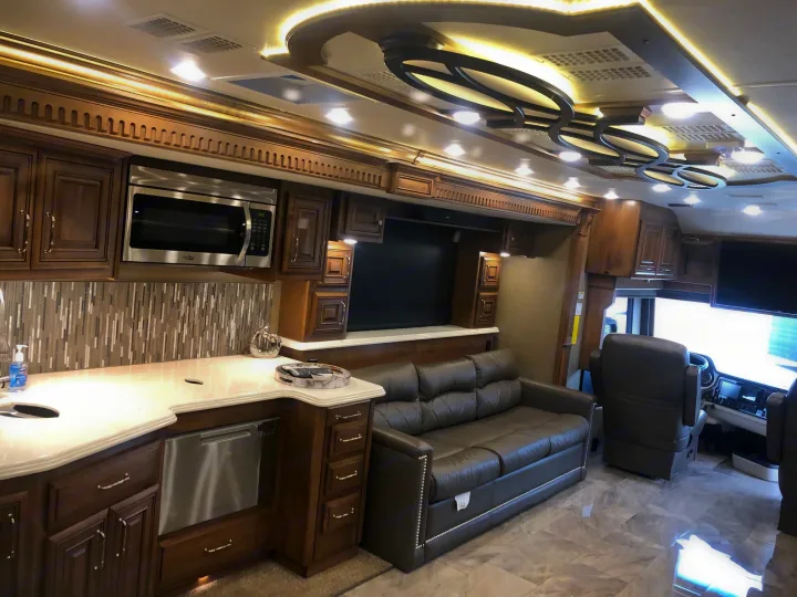 Luxurious RV rental interior shows a well-equipped kitchen area, sleek microwave, comfy leather sofa, and custom ceiling lighting.. Monaco Signature 2020