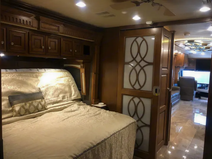 Luxurious RV rental bedroom with ornate wood cabinetry, plush bed, and elegant door leading to a spacious living area.. Monaco Signature 2020