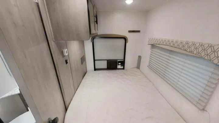 This RV rental bedroom features a comfy bed, wood-look cabinets, and a window with blinds.. Coachmen Freelander 2021