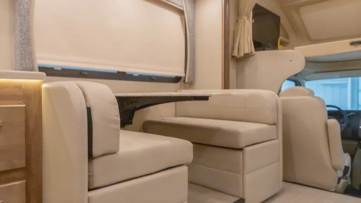 Clean and modern RV rental interior featuring a light-colored booth dinette with a table and a glimpse of the driver's cab.. Jayco Greyhawk prestige 30XP 2020
