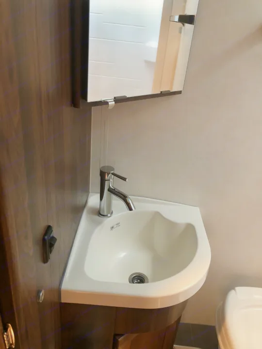 Compact RV rental bathroom featuring a corner sink, chrome faucet, and overhead mirrored cabinet.. Winnebago Mercedes Sprinter 2020
