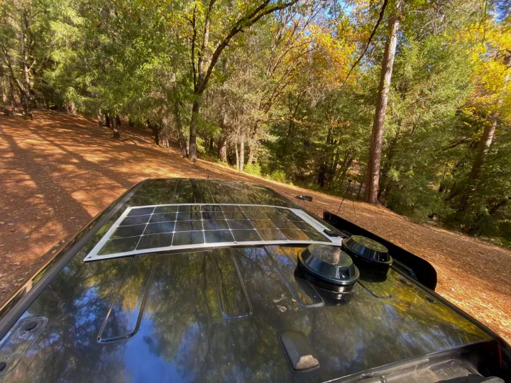 RV rental with a roof-mounted solar panel and gear, parked in a sun-dappled forest. Ready for your nature escape!. Dodge Ram Promaster City 2016