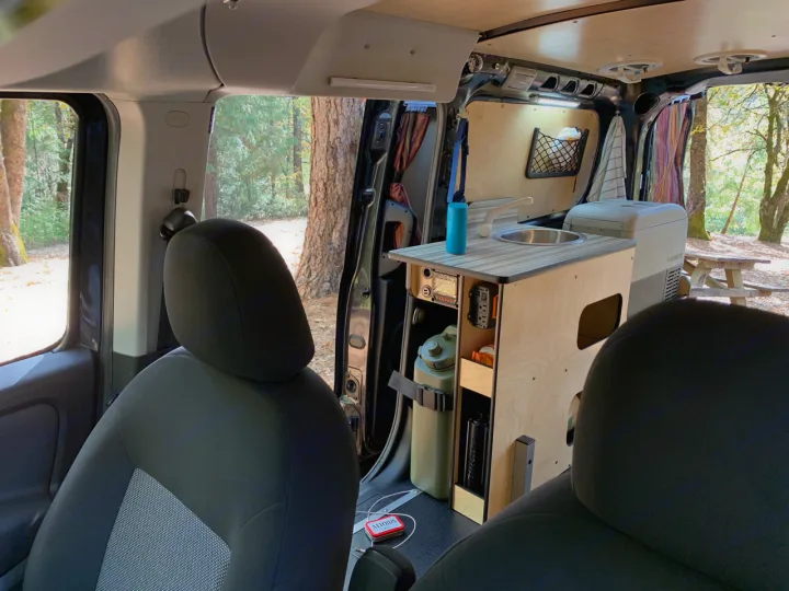 Compact RV rental interior featuring a custom kitchenette with sink, Dometic fridge, and built-in storage for travel adventures among trees.. Dodge Ram Promaster City 2016