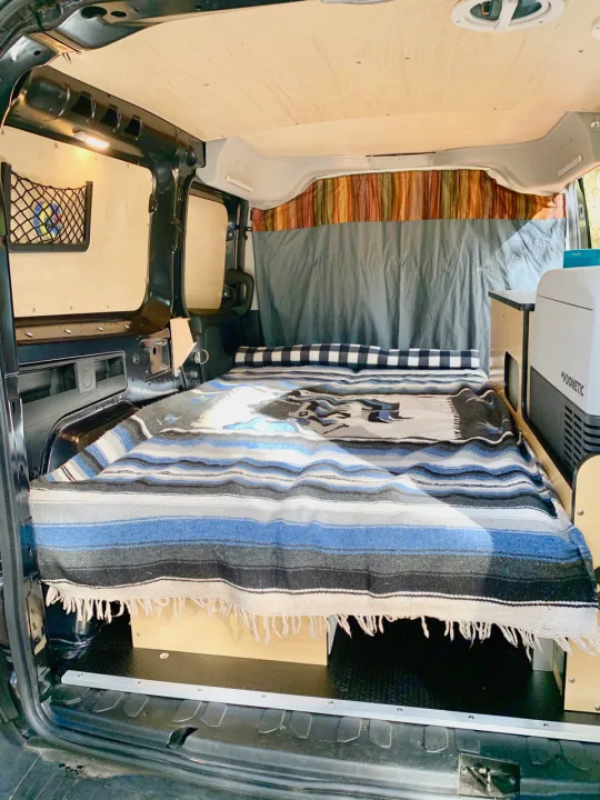 This RV rental's cozy camper van interior features a bed with storage, wood paneling, and a Dometic cooler.. Dodge Ram Promaster City 2016