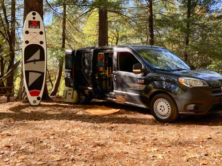 An Xterra SUP stands by a tree as a customized black Promaster City van offers cozy RV rental camping.. Dodge Ram Promaster City 2016