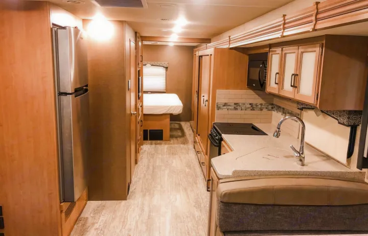 Interior of an RV rental, showcasing a modern kitchen with a fridge, sink, and stove, plus a bedroom area in the rear.. Other Hurricane 2019