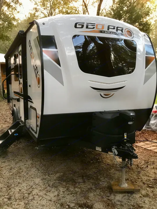 A white and black Geo Pro by Rockwood travel trailer RV rental is parked on a dirt lot amidst trees.. Other Other 2021