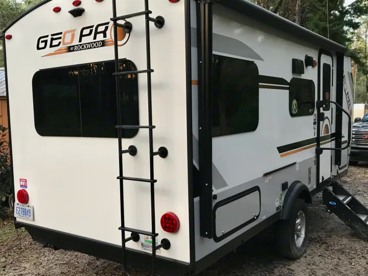 Compact white Geo Pro travel trailer RV rental parked outdoors, showing its rear with a ladder and Michigan license plate.. Other Other 2021
