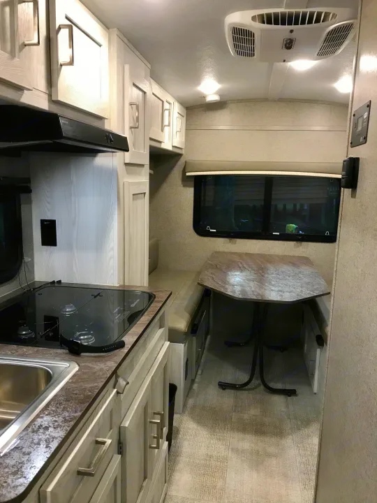 Explore this modern RV rental interior, featuring a compact kitchen with a sink and cooktop, dinette seating, and ceiling AC.. Other Other 2021