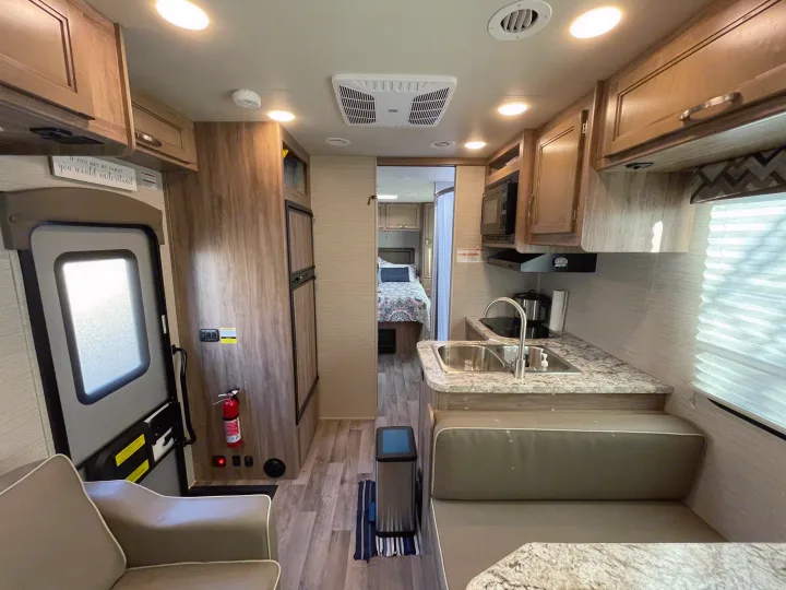 Explore this RV rental's cozy interior, featuring a kitchen with sink, dinette seating, and a comfortable bedroom. Ready for travel!. Jayco Redhawk 2020
