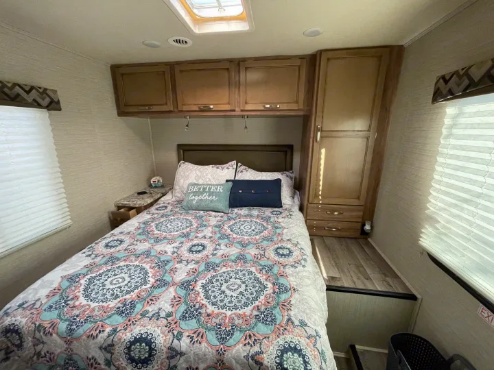 Cozy RV rental bedroom featuring patterned bedding, overhead cabinets, and a tall wardrobe. Ready for adventure!. Jayco Redhawk 2020