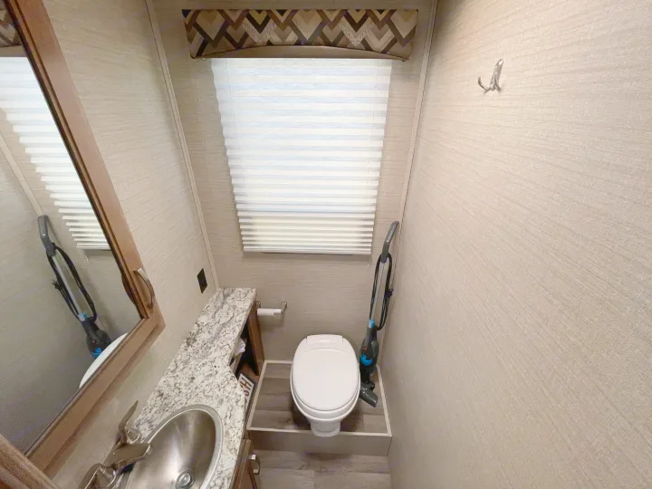 RV rental bathroom interior with compact toilet, sink, mirror, and small vacuum for tight spaces.. Jayco Redhawk 2020