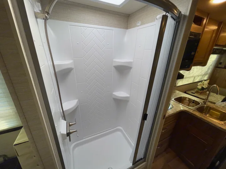 RV rental interior: compact shower with stylish herringbone pattern, built-in shelves, and adjacent kitchen area.. Jayco Redhawk 2020