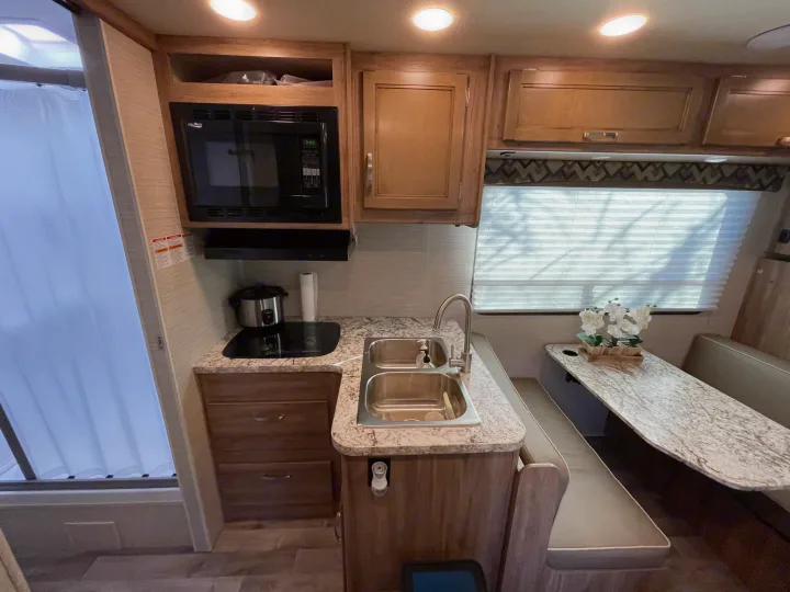 Modern RV rental interior: well-equipped kitchen with microwave, sink, & stove; comfy dinette seating perfect for travel.. Jayco Redhawk 2020