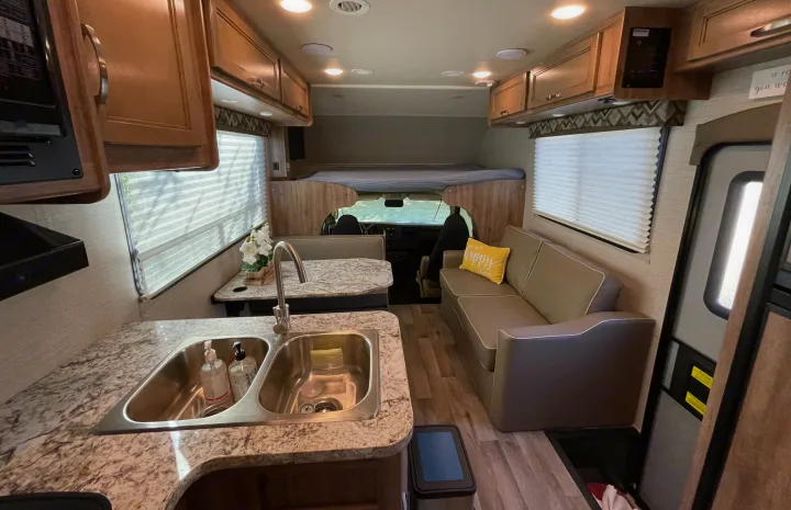 Modern RV rental interior with well-equipped kitchen, dining booth, sofa, and overhead bed, ready for adventures.. Jayco Redhawk 2020