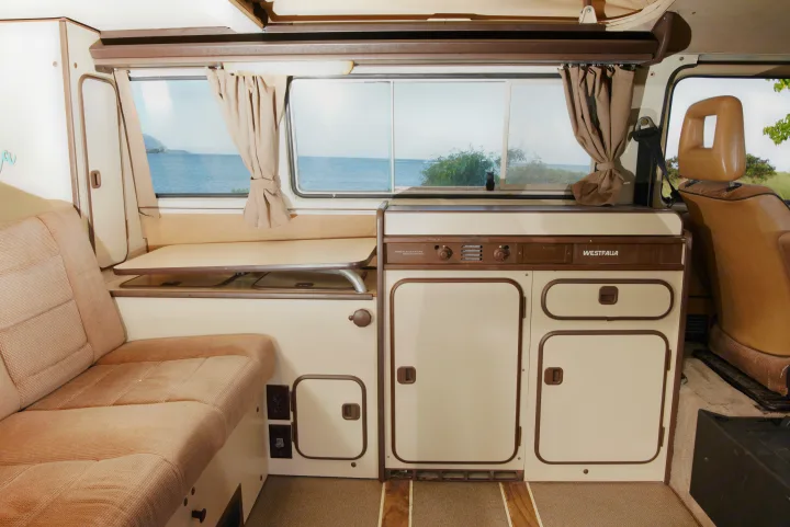 Explore a cozy Westfalia camper RV rental interior with a functional kitchenette, comfy seating, and ocean view.. Volkswagen Westfalia 1985