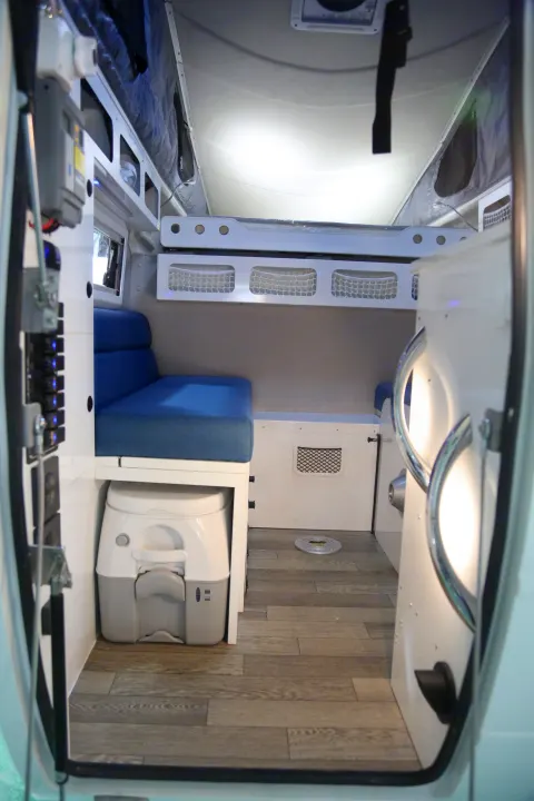 Cozy rv rental interior: features a blue cushioned bench, upper bunk, portable toilet, and wood flooring.. Other Other 2021