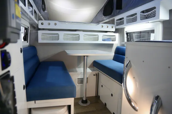 Spacious and modern RV rental interior featuring a comfortable dining area with blue benches, a table, and overhead bunk/storage.. Other Other 2021