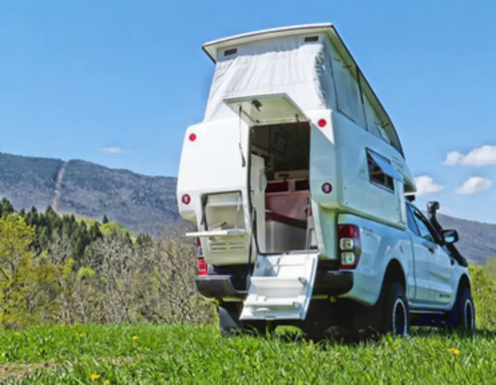 A white pickup truck with an open pop-top camper, ideal for an rv rental adventure, rests on a green hill near mountains.. Other Other 2021