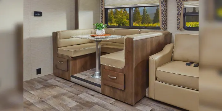 This RV rental interior shows a dinette booth with a table, comfortable seating, and large windows with forest views, perfect for travel.. Jayco Redhawk 2020