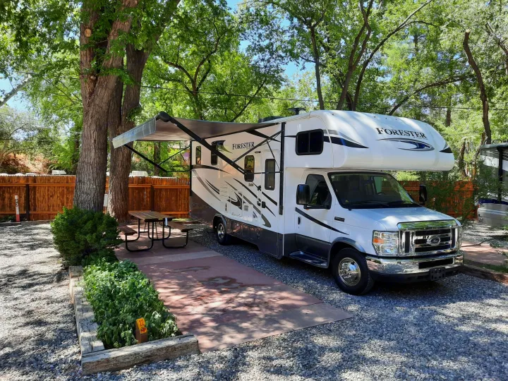A white Forester rv rental motorhome with an awning out, parked at a spacious, treed campsite.. Forest River Other 2018