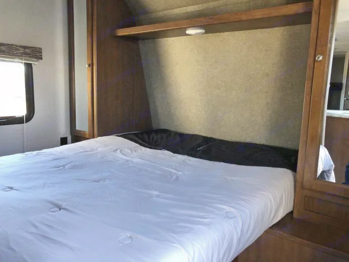 Experience comfort in this RV rental bedroom: A neatly made bed, overhead shelf, and built-in mirrored cabinet provide ample space.. Keystone Hideout 2018