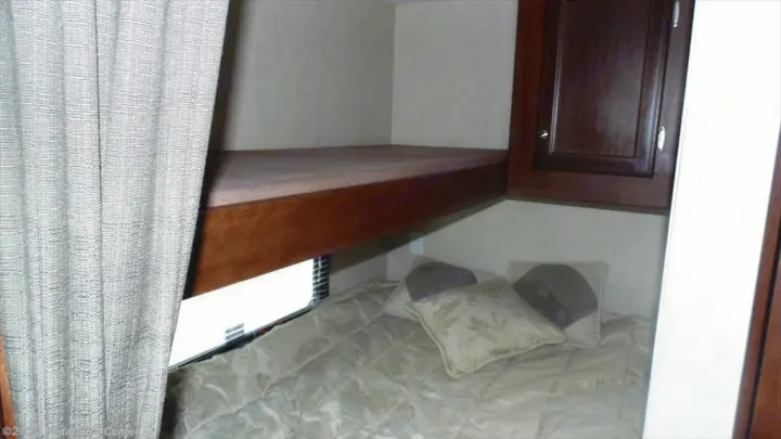 RV rental bedroom featuring a lower bed and upper bunk. A curtain is drawn, and a cabinet is on the right.. Eclipse Recreational Vehicles Milan 2013