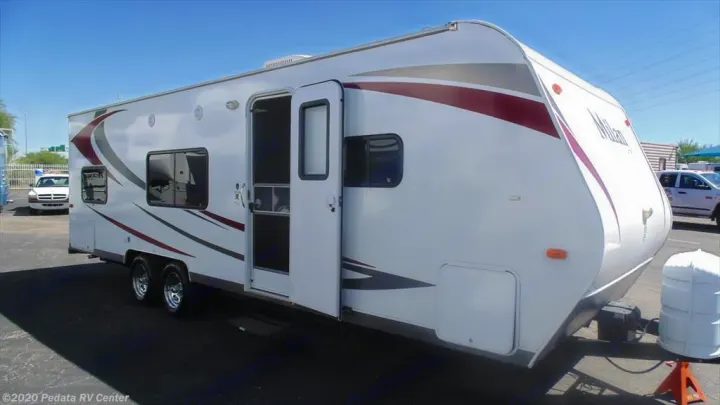 White travel trailer available for RV rental, showing its exterior with an open door and graphics, parked outdoors.. Eclipse Recreational Vehicles Milan 2013