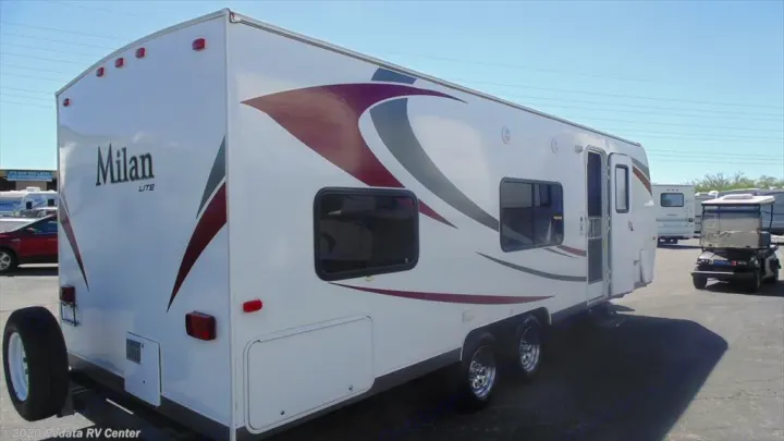 White Milan Lite travel trailer, a versatile RV rental option, with colorful decals and multiple windows, parked in an outdoor lot.. Eclipse Recreational Vehicles Milan 2013