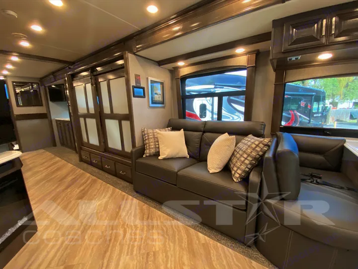 Spacious RV rental living area with a dark sofa, large windows, and built-in storage. Features modern flooring.. Fleetwood Pace Arrow 2021
