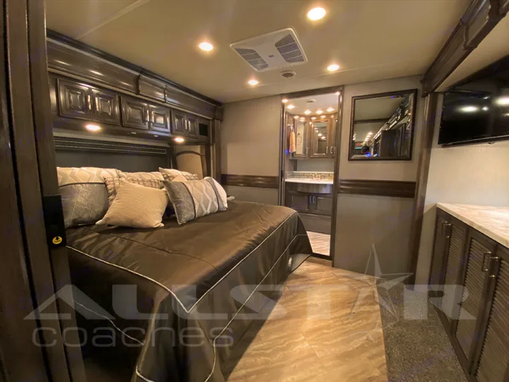 Luxury RV rental bedroom: Features a large bed, overhead cabinets, TV, and en-suite bathroom access. Perfect for travel comfort.. Fleetwood Pace Arrow 2021