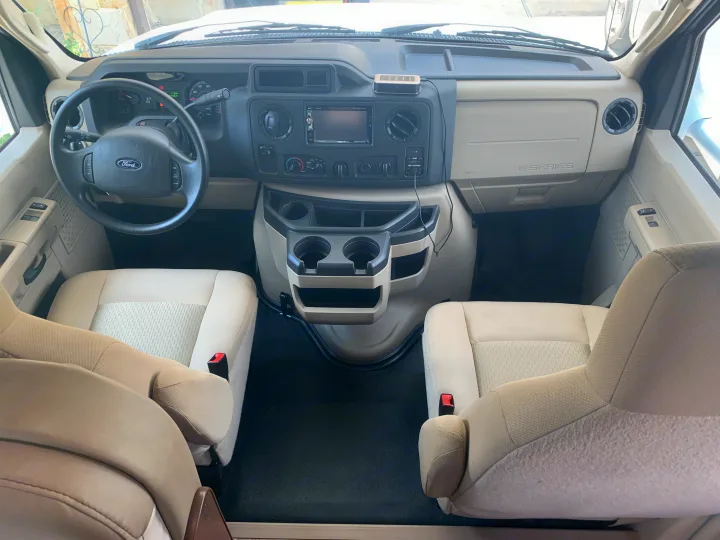 Ford E-Series RV rental cockpit. Features dashboard, steering wheel, cupholders, and tan front seats.. Thor Freedom Elite 2019