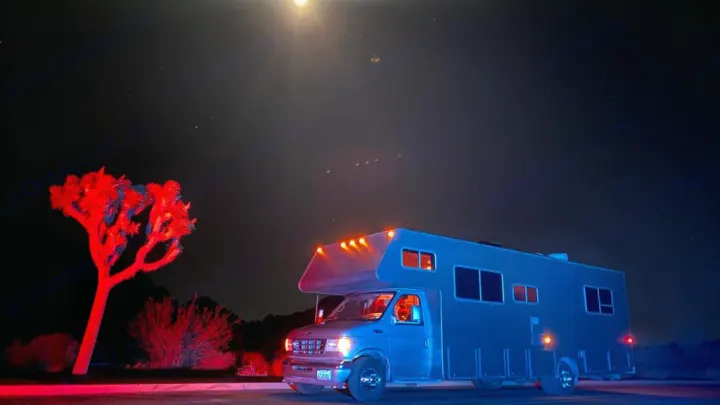 A striking blue RV rental under a starry desert night sky, beside a vivid red Joshua tree. Celestial lights visible above.. Jayco Greyhawk 2002