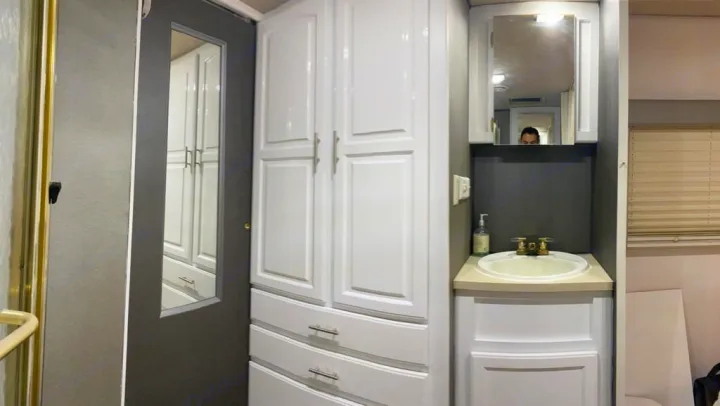 A well-organized RV rental bathroom featuring white storage cabinets, a mirrored door, and a clean sink vanity against dark walls.. Jayco Greyhawk 2002