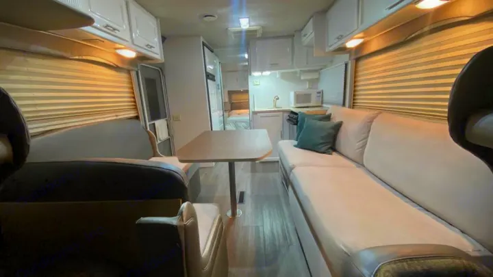 Spacious RV rental interior: living area with light-colored sofa, wooden dinette, kitchen, and a glimpse of the rear bedroom.. Jayco Greyhawk 2002