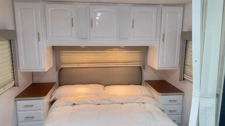 Cozy RV rental bedroom featuring bright white cabinets, comfy bed, and bedside storage for your journey.. Jayco Greyhawk 2002