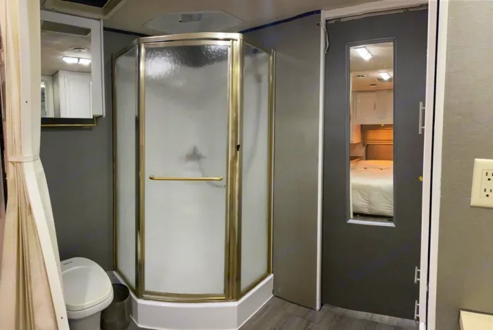 RV rental interior: a modern bathroom featuring a corner shower with frosted glass and a toilet, with a peek into the adjacent bedroom.. Jayco Greyhawk 2002