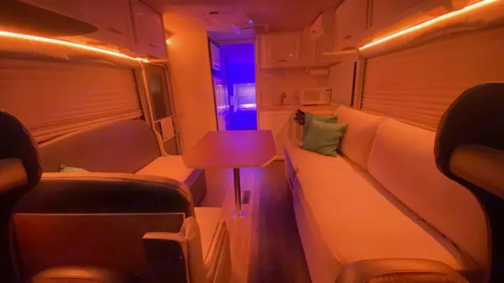 Cozy RV rental interior with dinette, kitchen, and blue-lit bedroom. Warm ambiance from LED strip lighting.. Jayco Greyhawk 2002