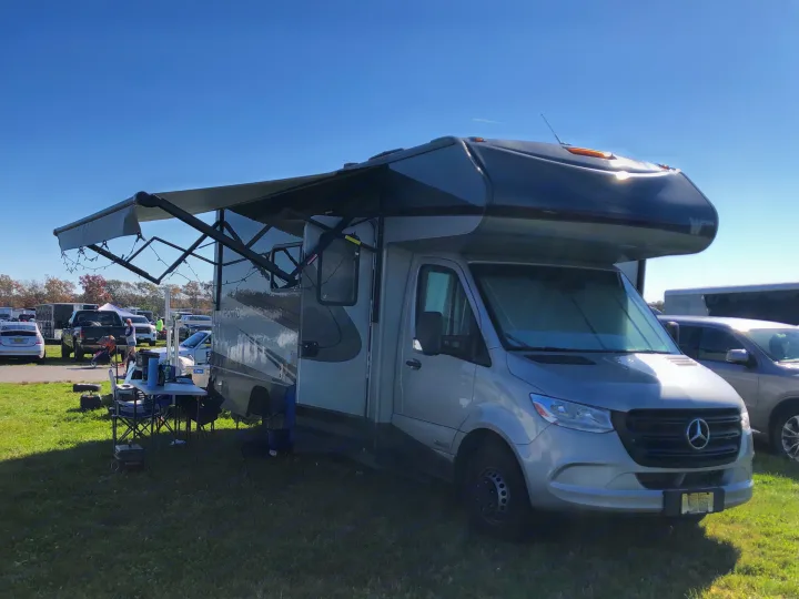 Silver Mercedes-Benz Sprinter RV rental with an extended awning and outdoor setup on grass under a clear blue sky.. Winnebago Mercedes Sprinter 2020