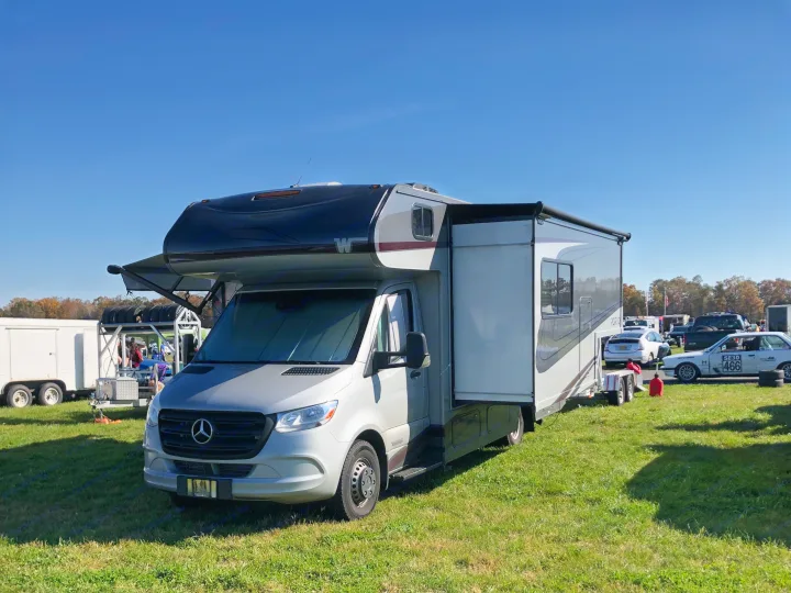 Silver Mercedes-Benz RV, perfect for an rv rental, parked on grass with awning & slide-out open at a sunny outdoor event.. Winnebago Mercedes Sprinter 2020