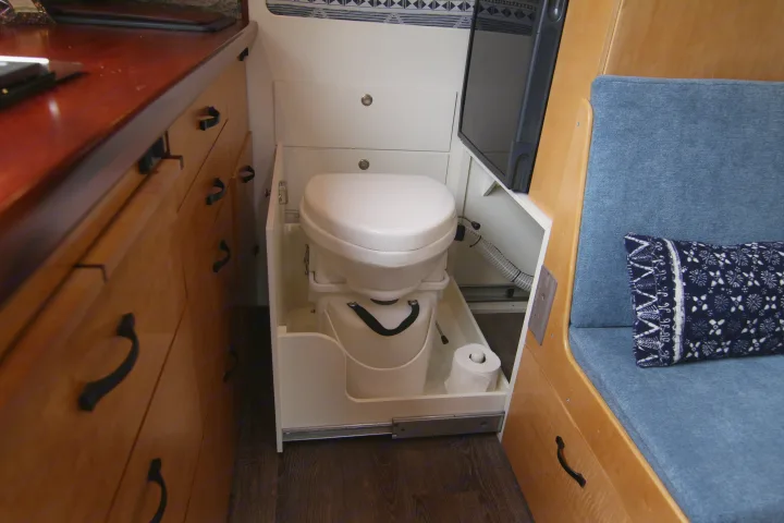 Compact RV rental interior reveals a clever pull-out toilet, wooden cabinetry, and blue seating for efficient space use.. Mercedes-Benz Sprinter 2012