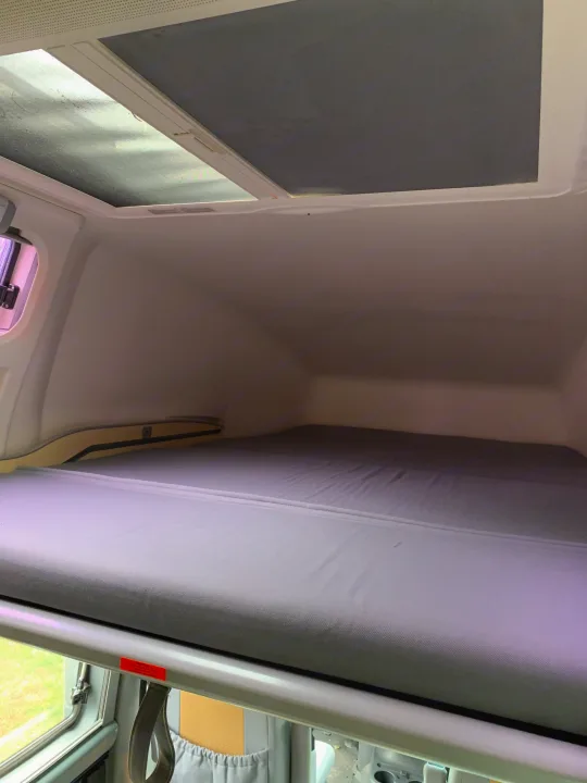 RV rental's cozy overhead bed with a grey mattress, dual skylights (one shaded), and a side window for camper trips.. Airstream Westfalia 2005