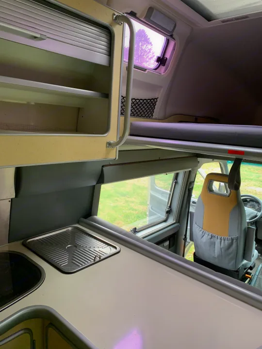 RV rental interior: Overhead bunk bed, kitchen sink, ample storage cabinets, and driver's seat for travel comfort.. Airstream Westfalia 2005